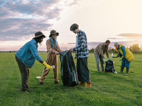 A diverse group of volunteers collecting trash in a field at sunset, promoting environmental awareness.