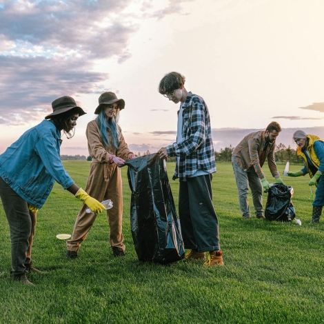 A diverse group of volunteers collecting trash in a field at sunset, promoting environmental awareness.